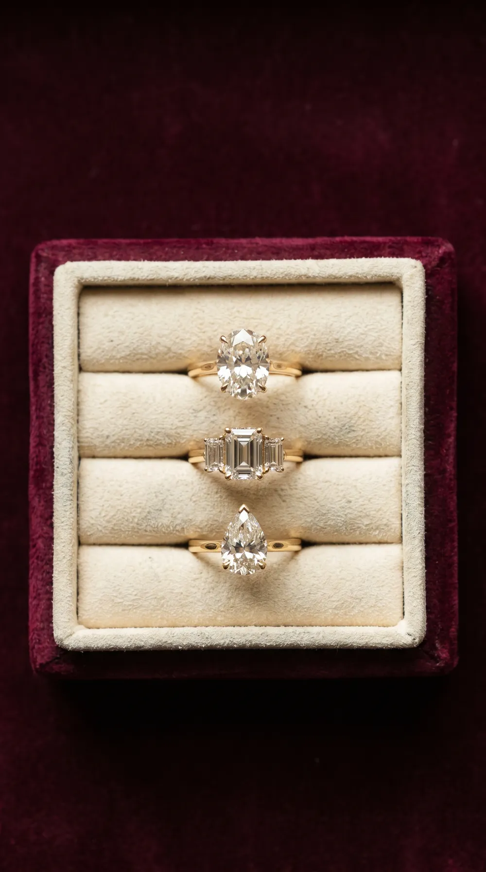 Three diamond engagement rings in a cream suede tray on burgundy velvet