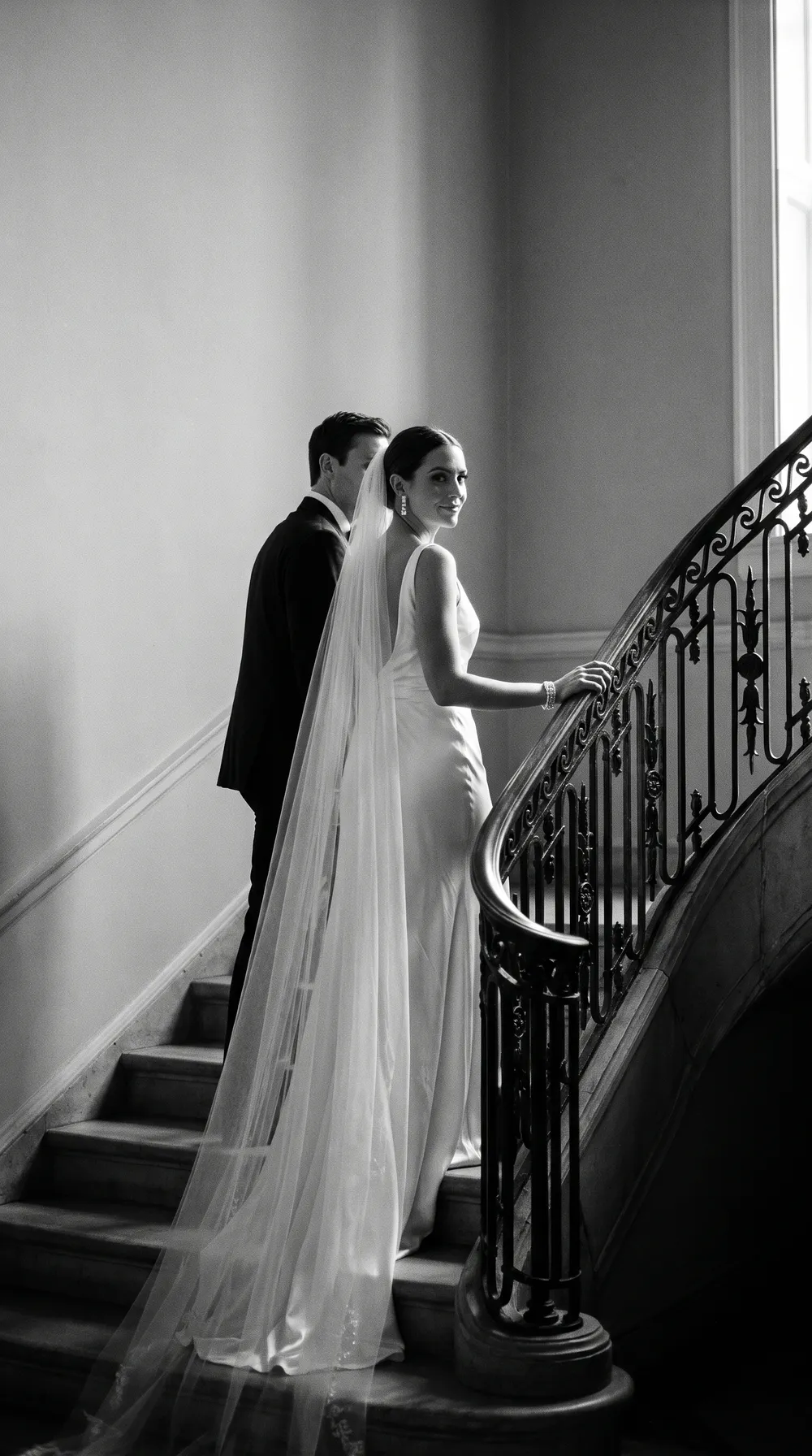 A bride and groom on a grand stone staircase, in black and white
