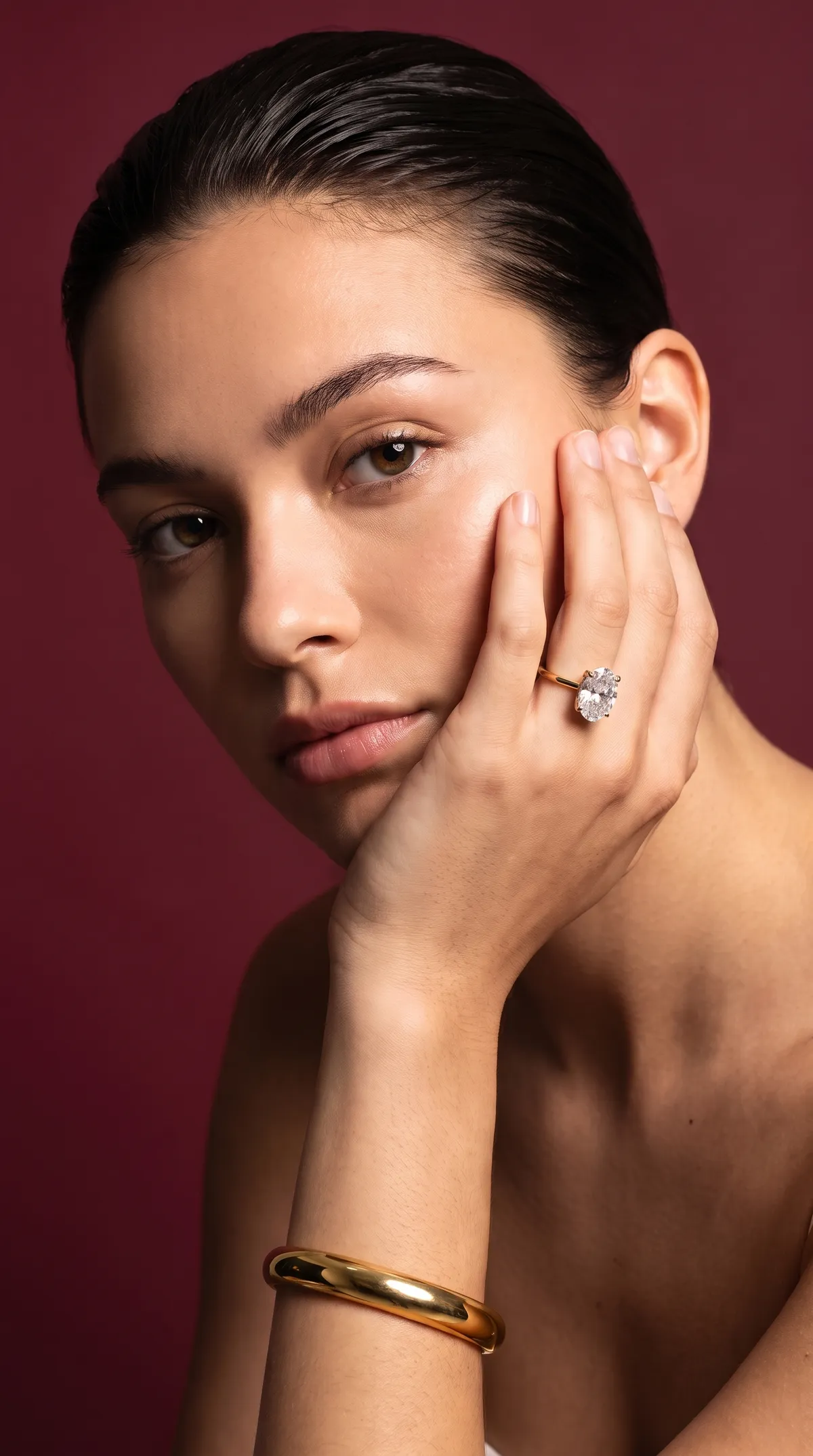 A model rests her cheek on her hand, wearing an oval diamond solitaire engagement ring in yellow gold