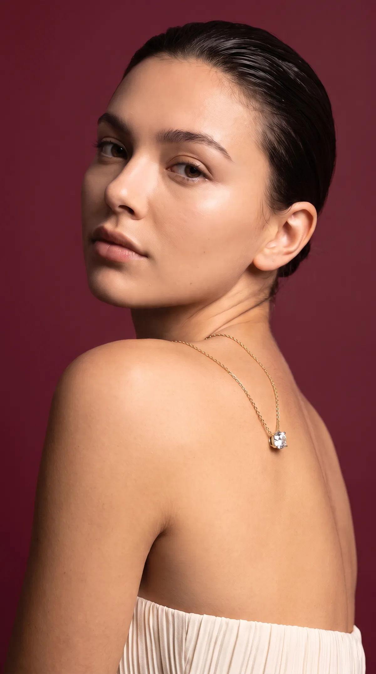 Looking back over her shoulder, wearing a round diamond solitaire pendant on a fine gold chain