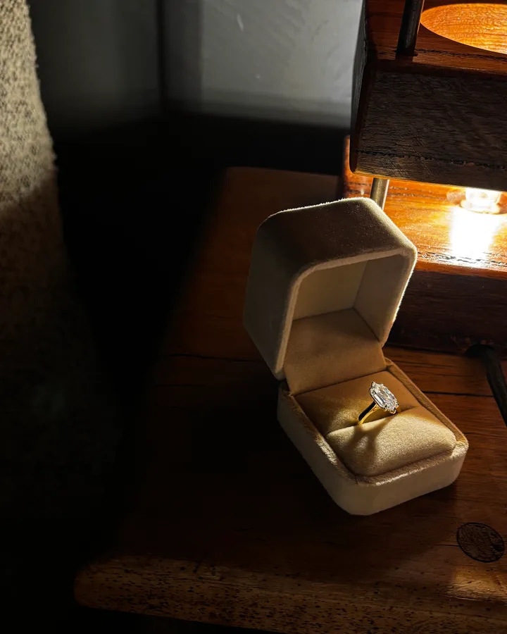 A diamond engagement ring in its velvet box on a wooden table